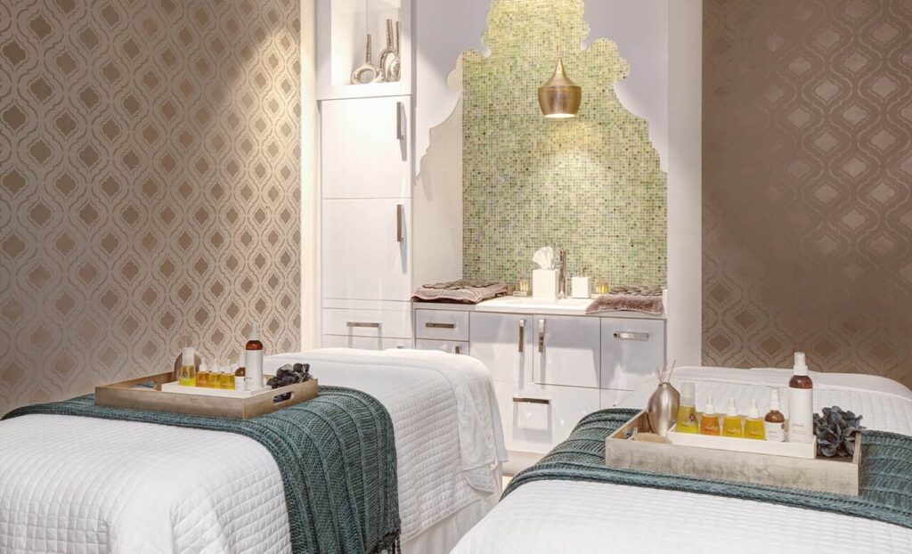 Light turquoise room with two white beds and massage oil ready for massaging