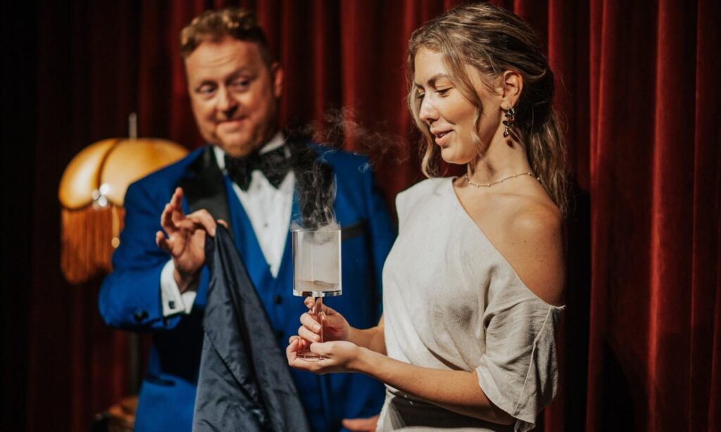 Bill Abbott reveals a smoke in glass magic trick to a surprised guest inside the velvet curtained Magic Hideaway showroom, St. Augustine Fl.