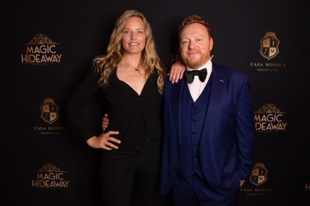 Bill and Rebecca Abbott posing in front of the Magic Hideaway photo wall.