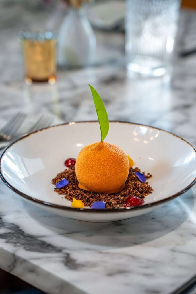 Orange mousse filled desert on a white dish and marble table at La Nouvelle, St. Augustine