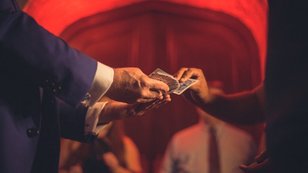 magician's hands holding out cards and guest's hand selecting card with red lit background