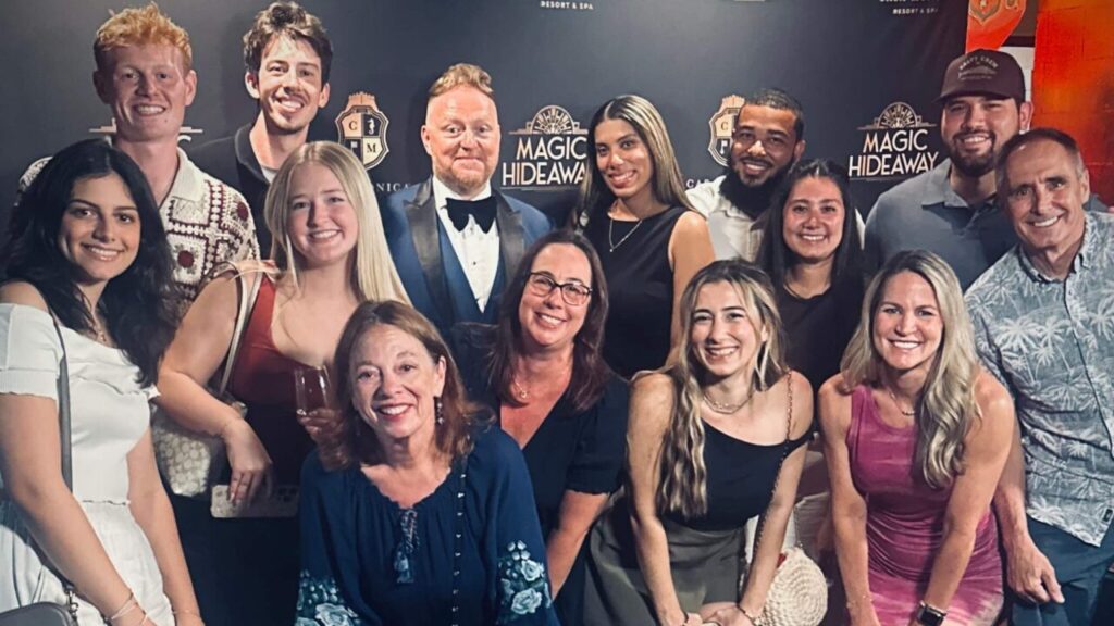 group of people standing and crouching in front of Magic Hideaway logo phot wall