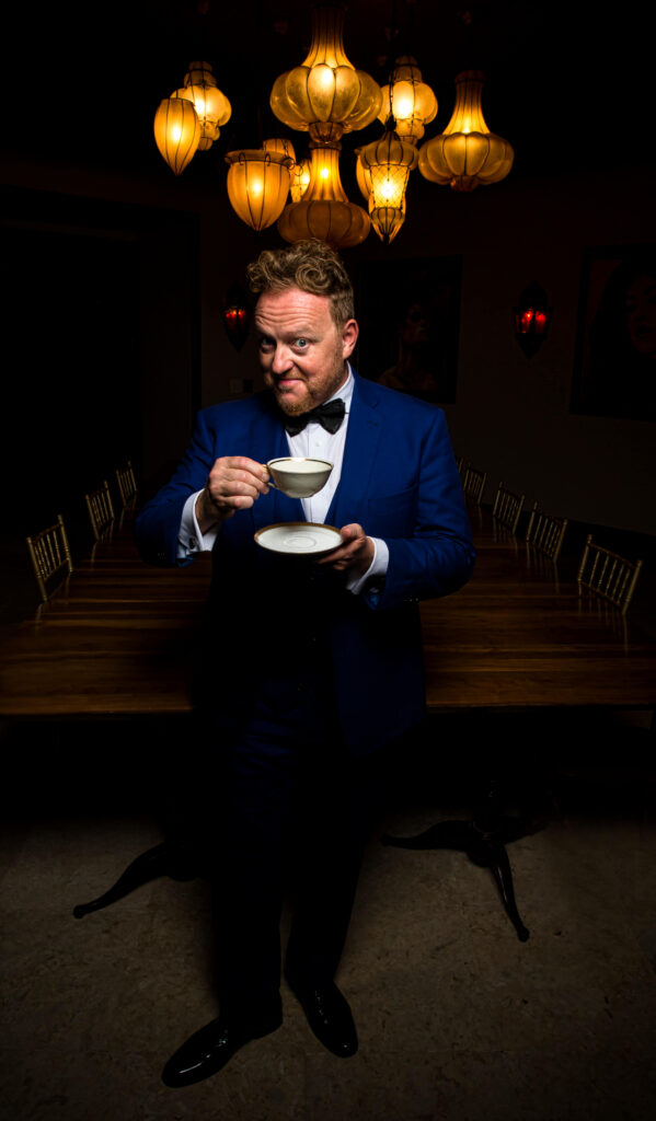 Magician in blue tuxedo holding tea cup and lantern overhead