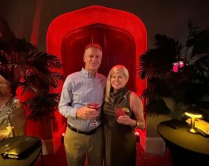 A couple dressed fancy in blue shirt and black dress hold cocktails in red lit doorway at theater
