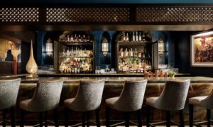 Sand colored bar chairs line bar with bottles displayed on wall behind