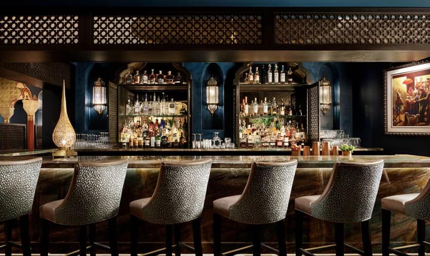 Sand colored bar chairs line bar with bottles displayed on wall behind