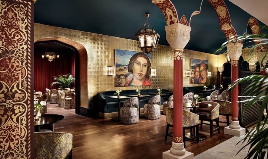 Gold leaf painted walled restaurant dining room with green velvet chairs and burgundy pillars
