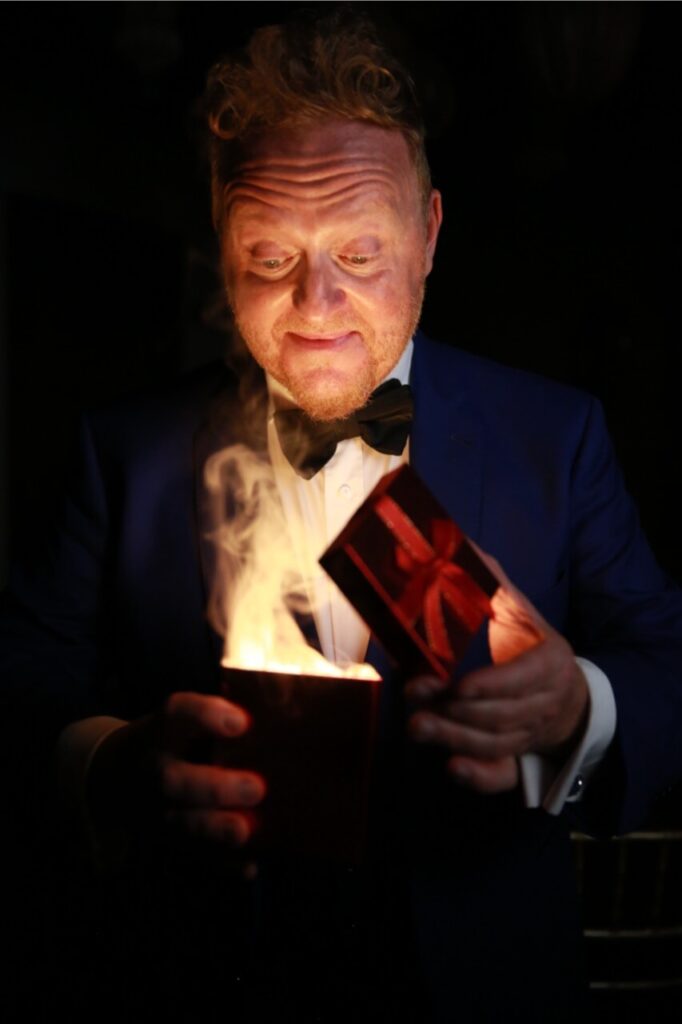 Man in blue tuxedo looking into a lit box, black background