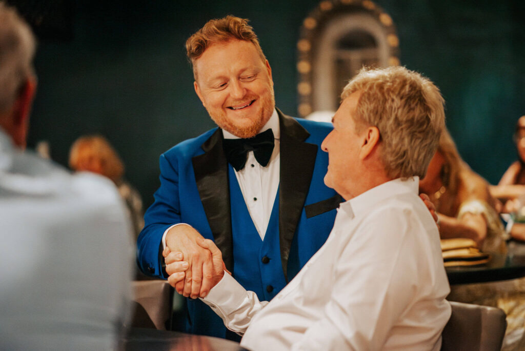 Bill Abbott in blue tuxedo shakes hands with guest in white dress shirt at Cordova chophouse bar