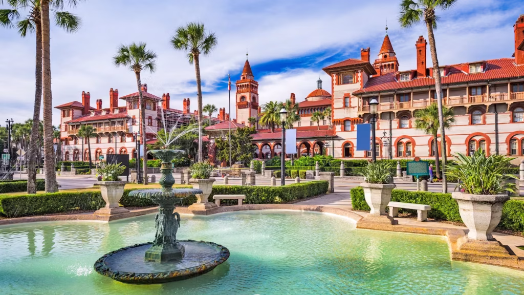 Red and sand colored Flagler College building in background teal fountain in foreground and bushes