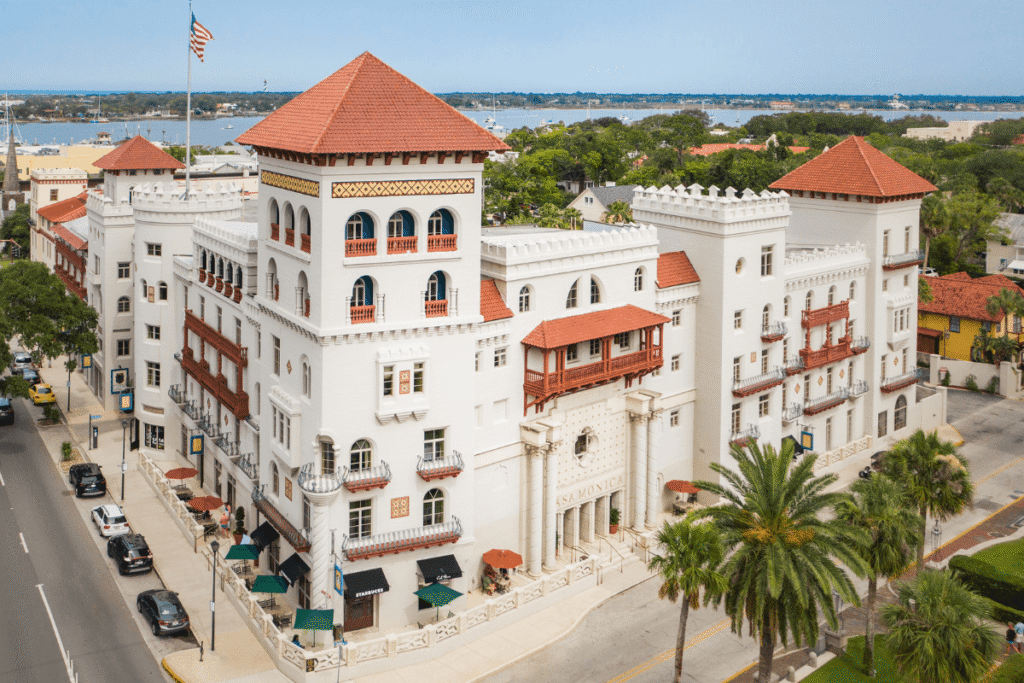 White building hotel, Casa Monica, with orange tile roof with car lined street and intercoastal in background