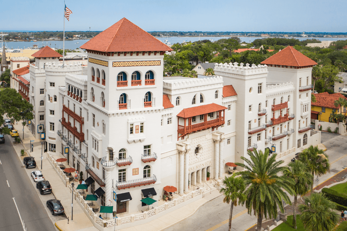 White building hotel, Casa Monica, with orange tile roof with car lined street and intercoastal in background