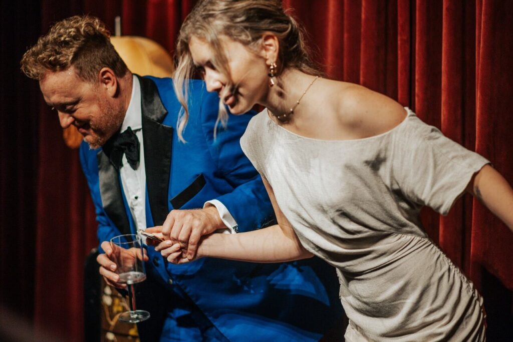 man in blue tuxedo and woman in tan dress bowing in front of red curtains