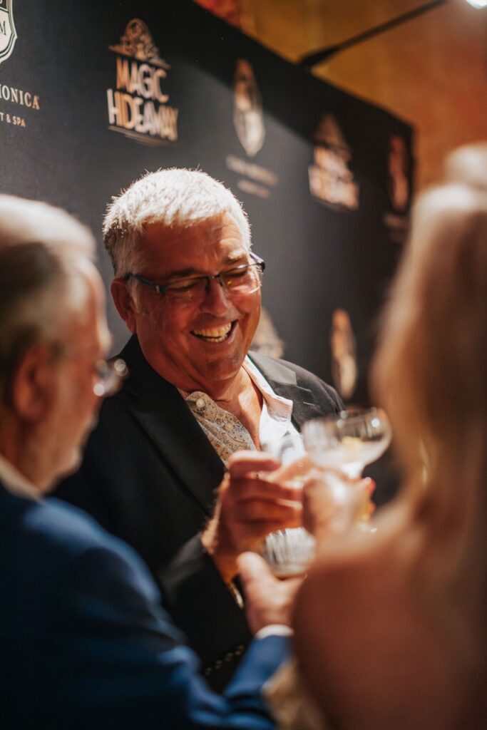 two gentlemen and a lady cheering their glasses and smiling in front of Magic Hideaway logo photo wall