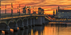 Sunset sky over Lion's Bridge in St. Augustine, with lights, water, and buildings.